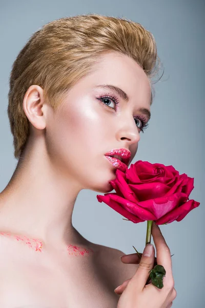 Low angle view of attractive woman with glitter on lips holding red rose isolated on grey — Stock Photo