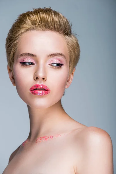 Jolie femme nue avec des paillettes sur le visage et le corps regardant loin isolé sur gris — Photo de stock