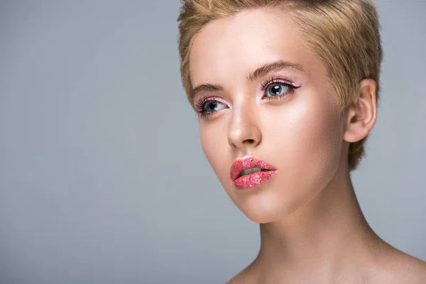 Atractiva mujer con brillo en los labios y pelo corto mirando hacia otro lado aislado en gris - foto de stock