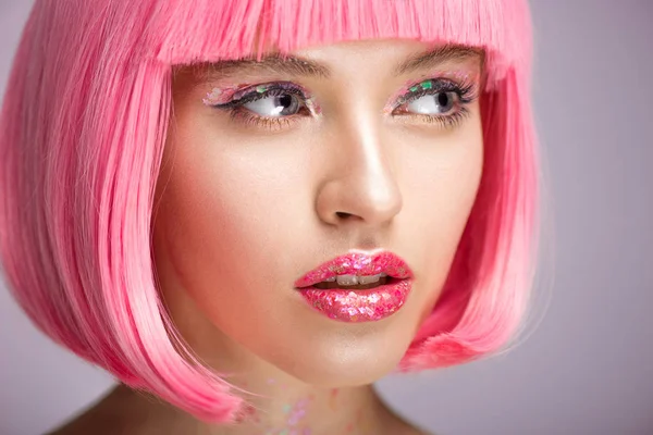 Tiro na cabeça de mulher atraente com cabelo rosa e brilho no rosto olhando para longe isolado em violeta — Fotografia de Stock