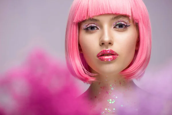 Attraktive Frau mit rosa Haaren und Glitzern im Gesicht, die vereinzelt in die Kamera auf violett blickt — Stockfoto