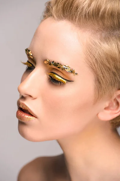 Side view of attractive woman with golden glitter on face isolated on grey — Stock Photo