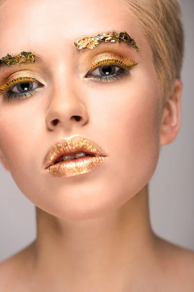 Mulher elegante atraente com brilho dourado no rosto olhando para a câmera isolada no cinza — Fotografia de Stock