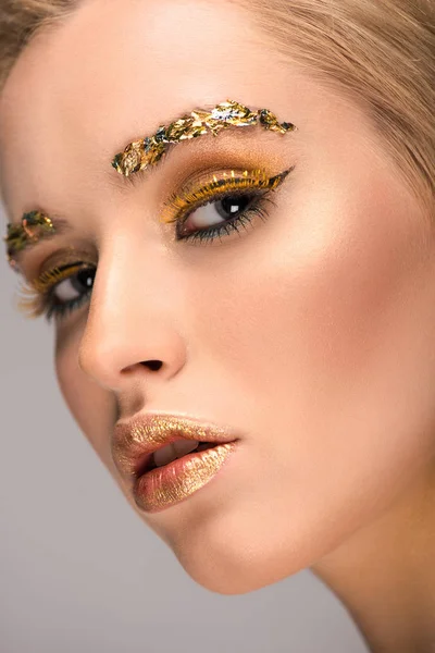 Headshot of attractive woman with golden glittering makeup looking at camera isolated on grey — Stock Photo