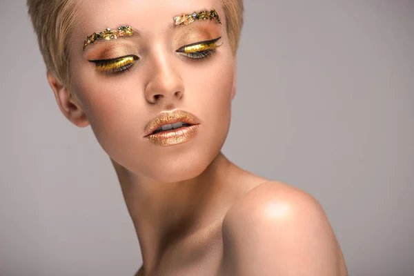 Jolie femme avec un maquillage doré brillant regardant vers le bas isolé sur gris — Photo de stock