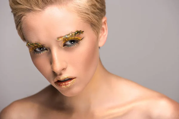 Atractiva mujer irritada con maquillaje brillante dorado aislado en gris - foto de stock