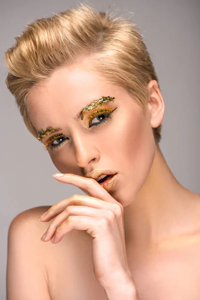 Attraktive Frau mit glitzerndem, stylischem Make-up, das die Lippen isoliert auf grau berührt — Stockfoto
