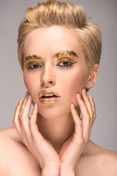 Attractive woman with golden bright makeup touching face isolated on grey — Stock Photo