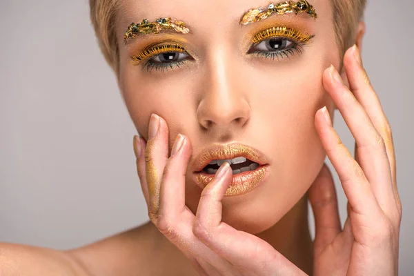 Attraktive Frau mit goldenem glitzerndem Make-up, das Gesicht isoliert auf grau berührt — Stockfoto