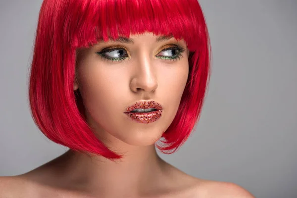 Retrato de mujer atractiva con el pelo rojo y brillo en la cara mirando hacia otro lado aislado en gris - foto de stock