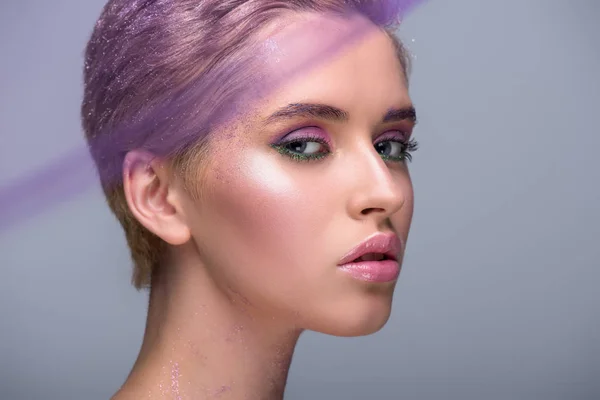 Attractive woman with violet makeup looking at camera isolated on grey — Stock Photo