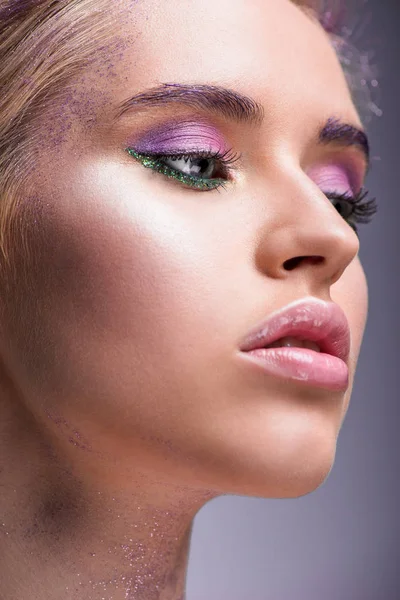 Headshot de jolie femme avec des paillettes violettes sur le cou regardant loin isolé sur violet — Photo de stock