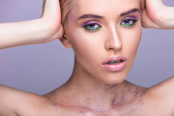 Beautiful woman with violet glitter on neck touching head isolated on violet — Stock Photo