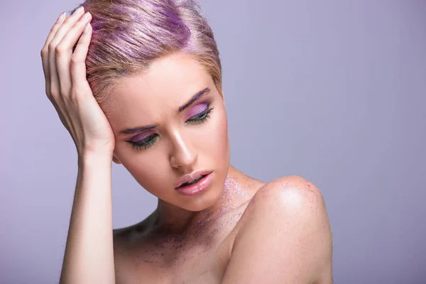 Hermosa mujer con brillo violeta en el cuello y pelo corto mirando hacia abajo aislado en violeta - foto de stock