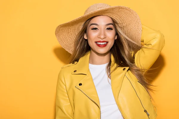 Sonriente elegante asiático mujer en paja sombrero en amarillo fondo - foto de stock