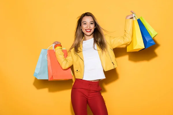 Sorridente donna asiatica elegante con borse della spesa su sfondo giallo — Foto stock