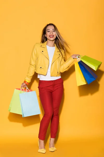 Happy asian female shopaholic with paper bags on yellow background — Stock Photo