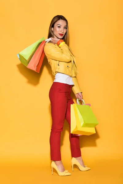 Asian young woman with shopping bags on yellow background — Stock Photo