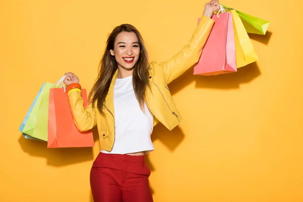 Sonriente asiático mujer con compras bolsas en amarillo fondo - foto de stock