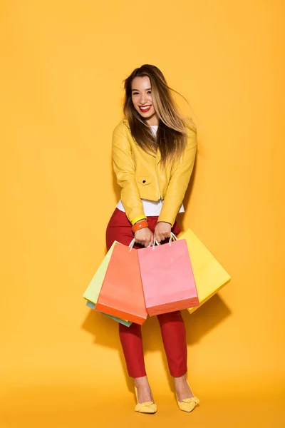 Smiling asian woman with shopping bags on yellow background — Stock Photo