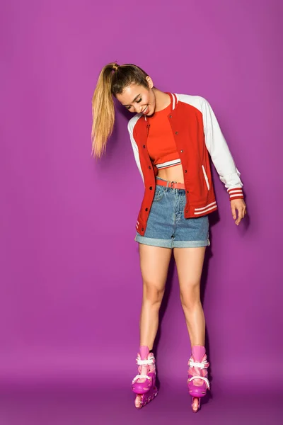 Beautiful happy asian girl standing in roller skates and looking down isolated on violet — Stock Photo