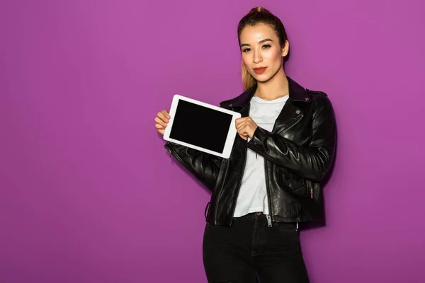 Hermosa mujer asiática joven sosteniendo tableta digital con pantalla en blanco y mirando a la cámara aislada en violeta - foto de stock