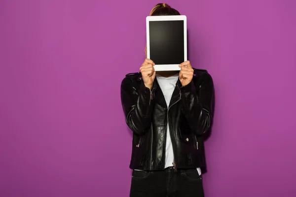 Jovem elegante em jaqueta de couro escondendo rosto com tablet digital isolado em violeta — Fotografia de Stock