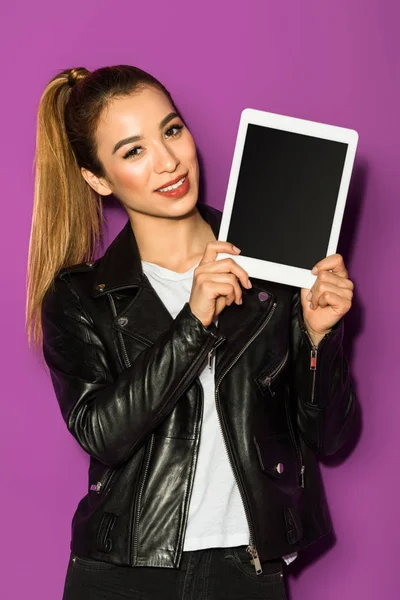 Beautiful asian girl holding digital tablet with blank screen and smiling at camera isolated on violet — Stock Photo