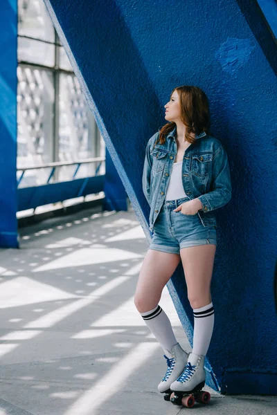 Задумчивая стильная женщина в джинсовой одежде, высоких носках и ретро роликовых коньках смотрит в сторону — стоковое фото