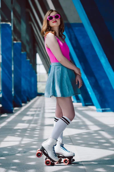 Jeune femme élégante en vêtements à la mode, lunettes de soleil rétro, chaussettes hautes et patins à roulettes debout au parking — Photo de stock