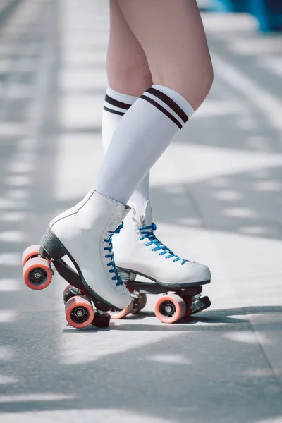 Partial view of woman in white high socks with black stripes and retro roller skates — Stock Photo