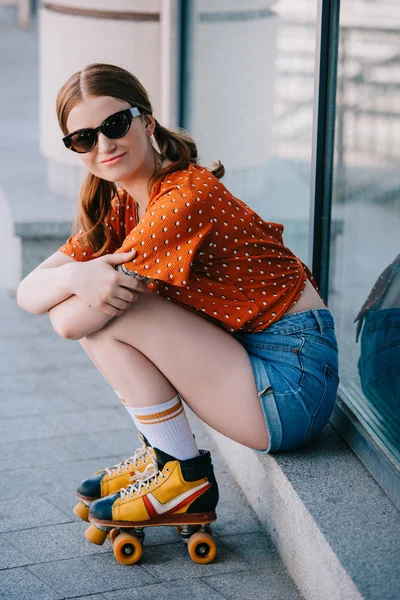 Schönes stylisches Mädchen mit Sonnenbrille und Rollschuhen, das auf der Treppe sitzt und in die Kamera lächelt — Stockfoto