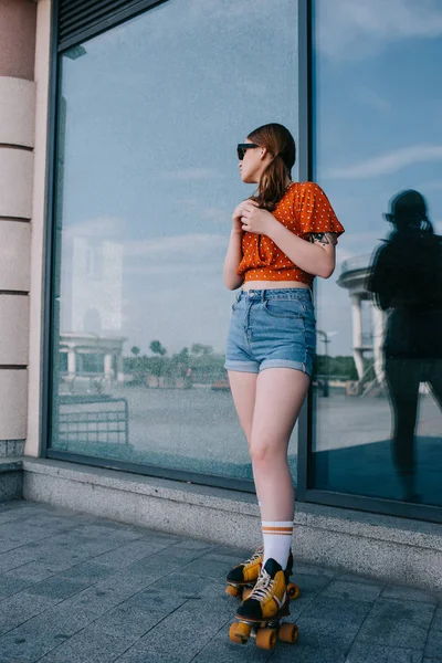 Bela menina elegante em patins de pé e olhando para longe na rua — Fotografia de Stock