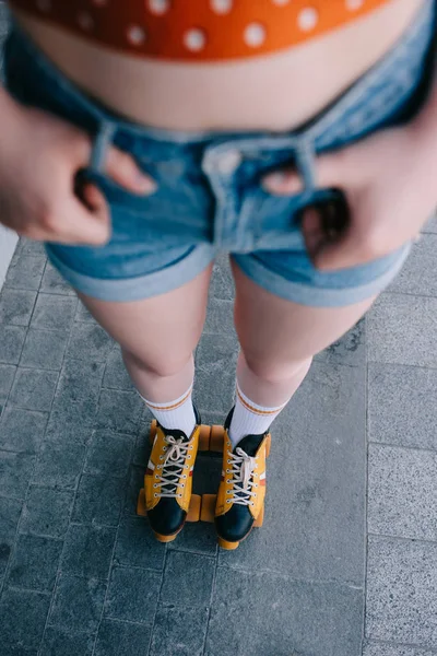 Recortado disparo de chica en pantalones cortos de mezclilla y patines de pie en la calle - foto de stock