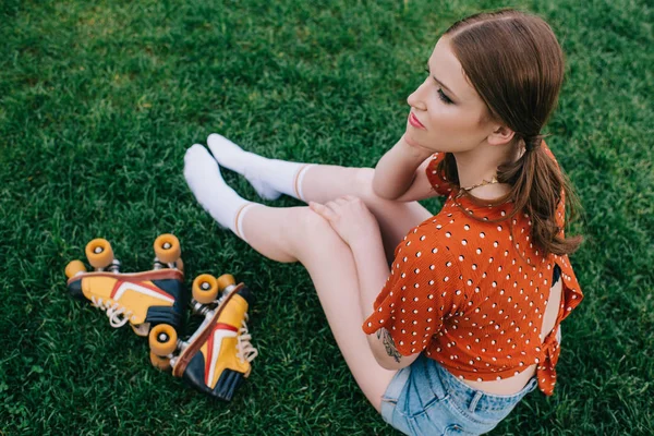 Високий кут зору дівчини з ковзанами, сидячи на траві і дивлячись — стокове фото
