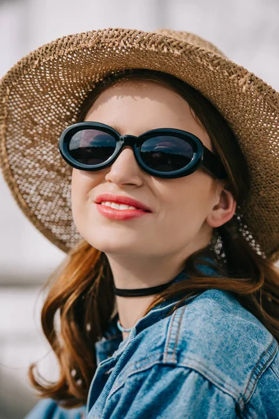 Portrait of happy young woman in sunglasses, hat and denim jacket smiling outdoors — Stock Photo