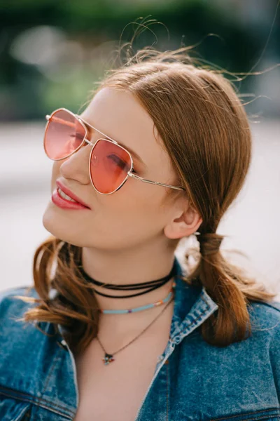 Портрет красивой улыбающейся девушки в солнцезащитных очках и джинсовой куртке, смотрящей на улицу — Stock Photo