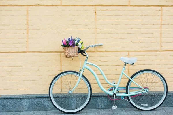 Vélo blanc avec de belles fleurs colorées dans le panier près du mur — Photo de stock