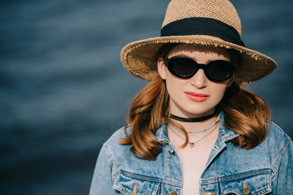 Portrait de belle jeune femme élégante en chapeau et lunettes de soleil regardant la caméra — Photo de stock