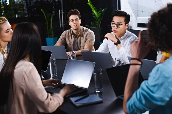 Groupe multiculturel de partenaires d'affaires ayant une discussion à table avec des ordinateurs portables dans le bureau moderne — Photo de stock