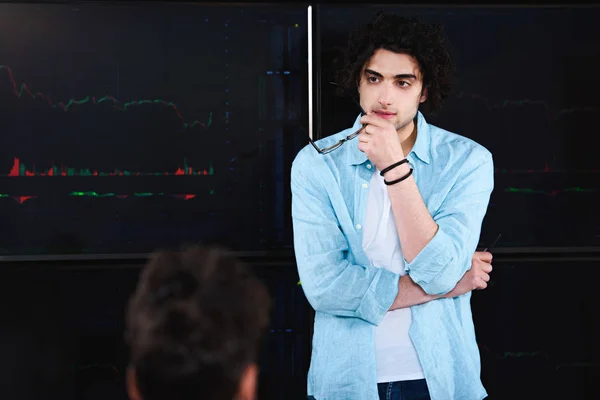 Young businessman with eyeglasses in hand standing in front of board with graphics at modern office — Stock Photo