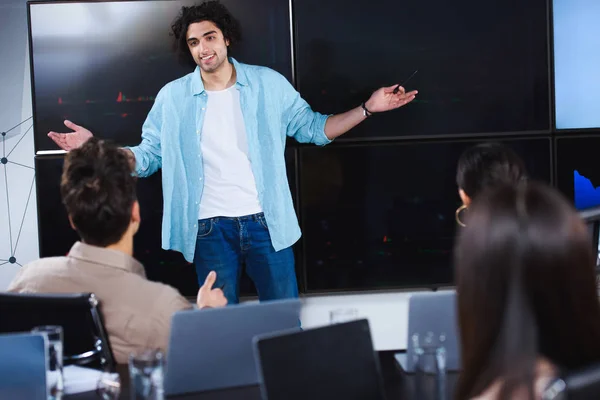 Lächelnder junger Geschäftsmann mit breiten Armen zeigt Geschäftspartnern Präsentation im modernen Büro — Stockfoto
