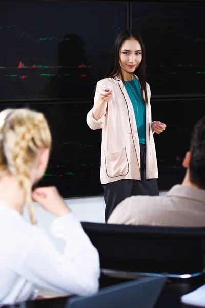 Asiatico businesswoman mostrando presentazione e puntando su femmina collega a moderno ufficio — Foto stock