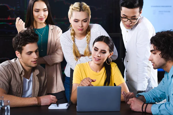 Joven empresaria señalando en la pantalla del ordenador portátil a los colegas en la oficina moderna - foto de stock