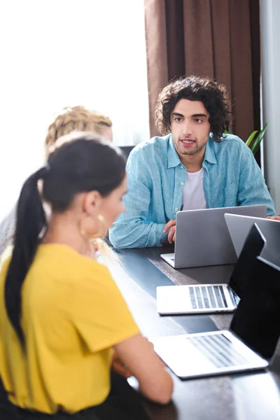 Jungunternehmer im Gespräch mit Partnerinnen am Tisch mit Laptops im modernen Büro — Stockfoto
