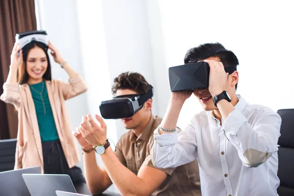 Dos hombres de negocios sonrientes usando auriculares de realidad virtual en la oficina moderna - foto de stock
