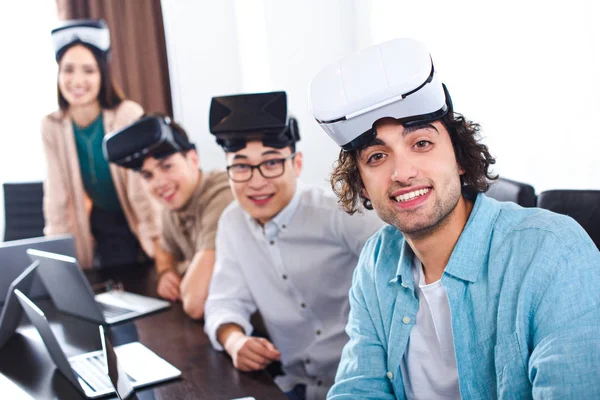 Group of multiethnic business partners with virtual reality headsets at table with laptops in modern office — Stock Photo
