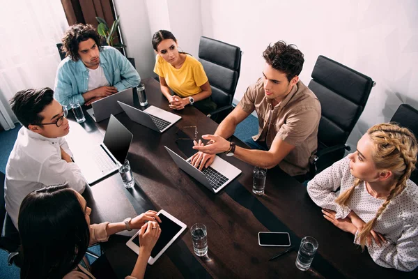 Vista ad alto angolo dei partner commerciali multiculturali che si riuniscono a tavola con i computer portatili in un ufficio moderno — Foto stock