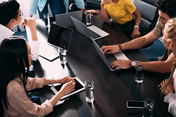 Cropped shot of multicultural business partners having meeting at table with laptops in modern office — Stock Photo