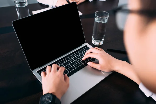 Recortado disparo de hombre de negocios escribiendo en el ordenador portátil con pantalla en blanco en la mesa con vaso de agua - foto de stock